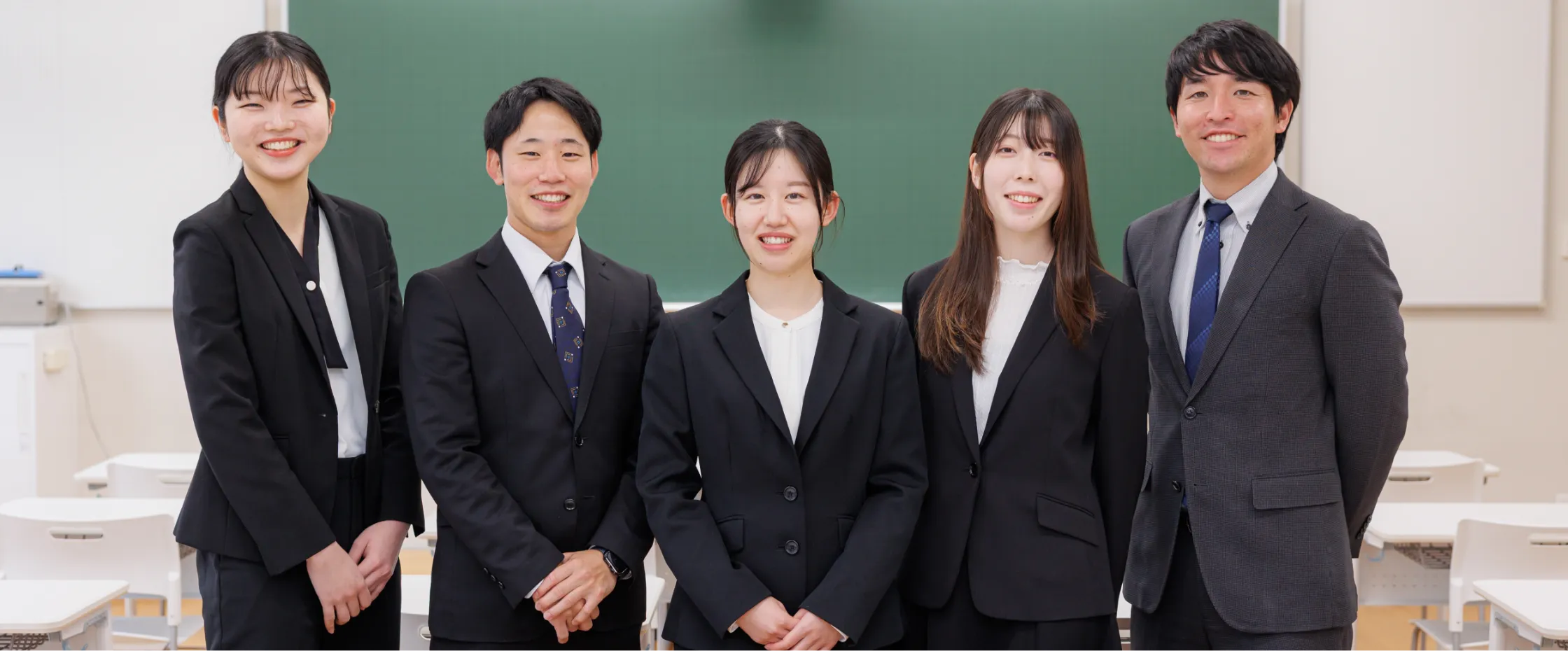 教室に並ぶ教員スタッフが、学生の成長を支える教育体制を伝える集合写真