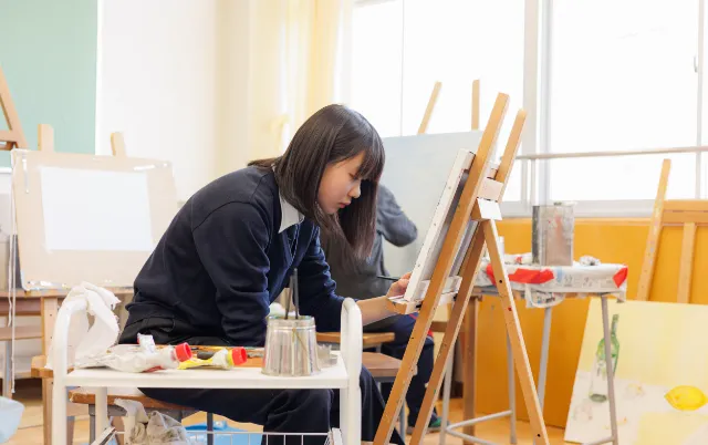 キャンバスに向かい、イーゼルで絵を描いている美術部の部員