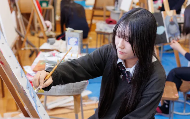 筆を使ってキャンバスに色を重ねている美術部の部員