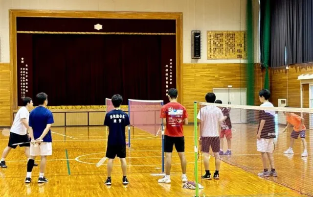 屋内の体育館で、バドミントン部の部員がコートに並んでいる様子
