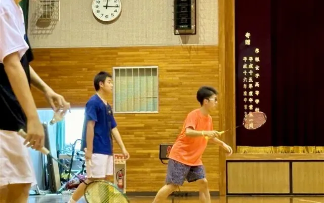 屋内の体育館で、バドミントン部の部員が試合形式でプレーしている様子