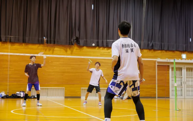 屋内の体育館で、バドミントン部の部員がラリーをしている様子