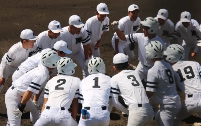 野球場で、ユニフォーム姿の野球部員が円陣を組んでいる様子