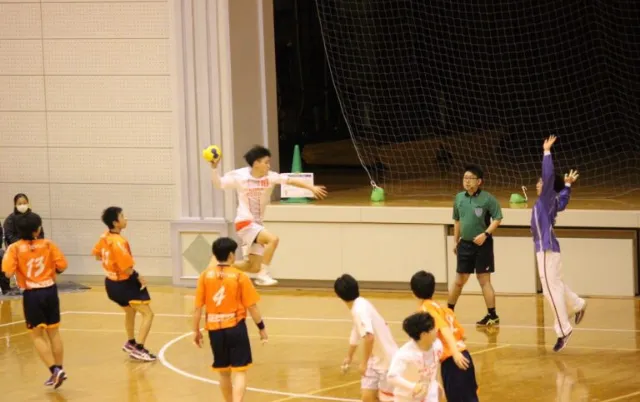 屋内の体育館で、ハンドボール部の部員がボールを使って練習している様子