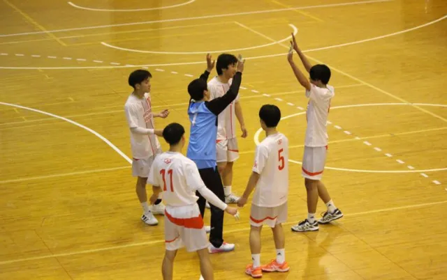 屋内の体育館で、ハンドボール部の部員が円になって集まっている様子