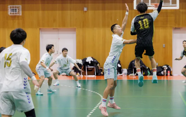 屋内の体育館で、ハンドボール部の部員がジャンプしてシュート動作をしている様子