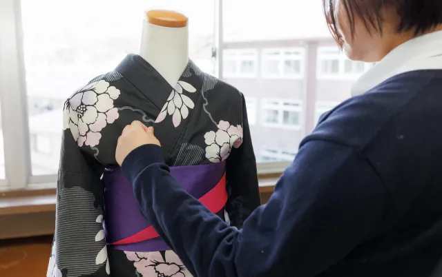 トルソーに着物を着せ、襟元の形を整えている部員の様子