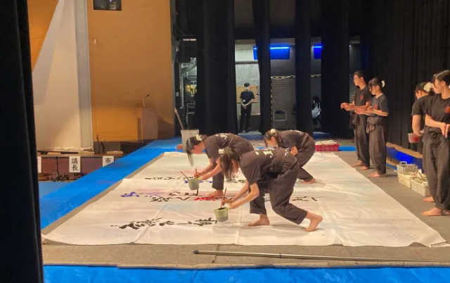 ステージ上で、部員が大きな紙に筆を入れている様子