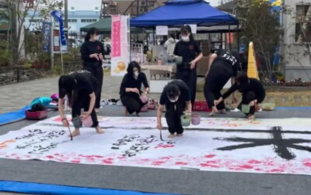 屋外イベントで、部員が大きな紙に揮毫している様子