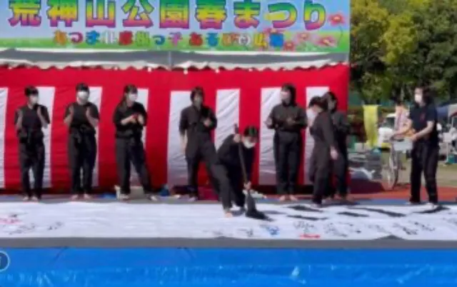 イベント会場で、部員が大きな筆で揮毫している様子