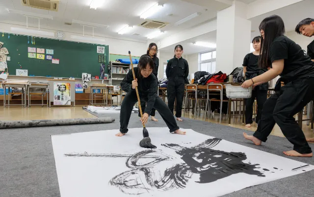 教室で、大きな紙に大筆で制作している様子
