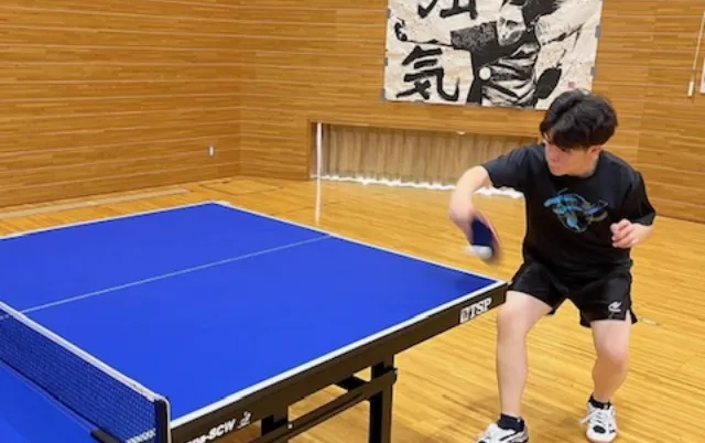 卓球台の前で、部員がラケットを振ってボールを打っている様子