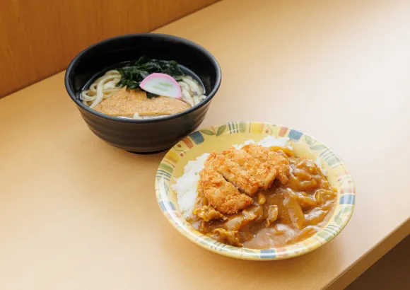 食堂のテーブルの上に置かれた、カレーライスとうどんの食事の例